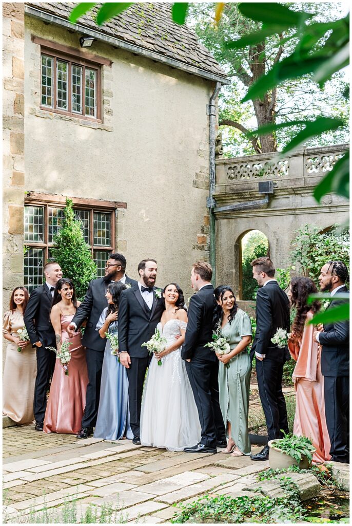 A bride and groom pose with their black tie attired groomsmen and mismatched bridesmaids for portraits at Virginia House in Richmond, serving as the enchanting, fairytale estate wedding venue. Photos by a Richmond wedding Photographer, Emily Nicole Photography.