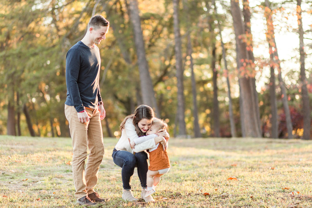 Everleigh runs to give mom and dad a hug during their couple poses in their fall session at Fort Ward Park in Alexandria, VA.