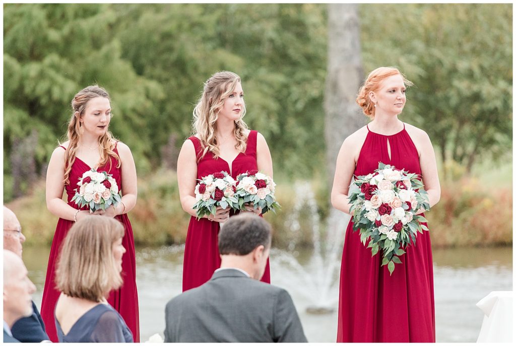How to choose your maid of honor. How to choose your matron of honor.
Three bridesmaids in burgundy red dresses standing at the alter at a ceremony, holding wood flower bouquets. Taken by Virginia wedding photographer Emily Nicole Photography.