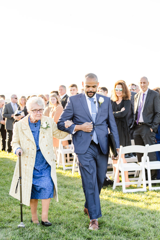 A groomsman walks the Grandmother of the Bride down the aisle during a wedding processional. Click to read more tips on wedding procession order from a Virginia wedding photographer.