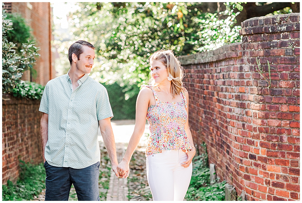 Wales Alley in Old Town Alexandria, couple looks at each other and holds hands in engagement session