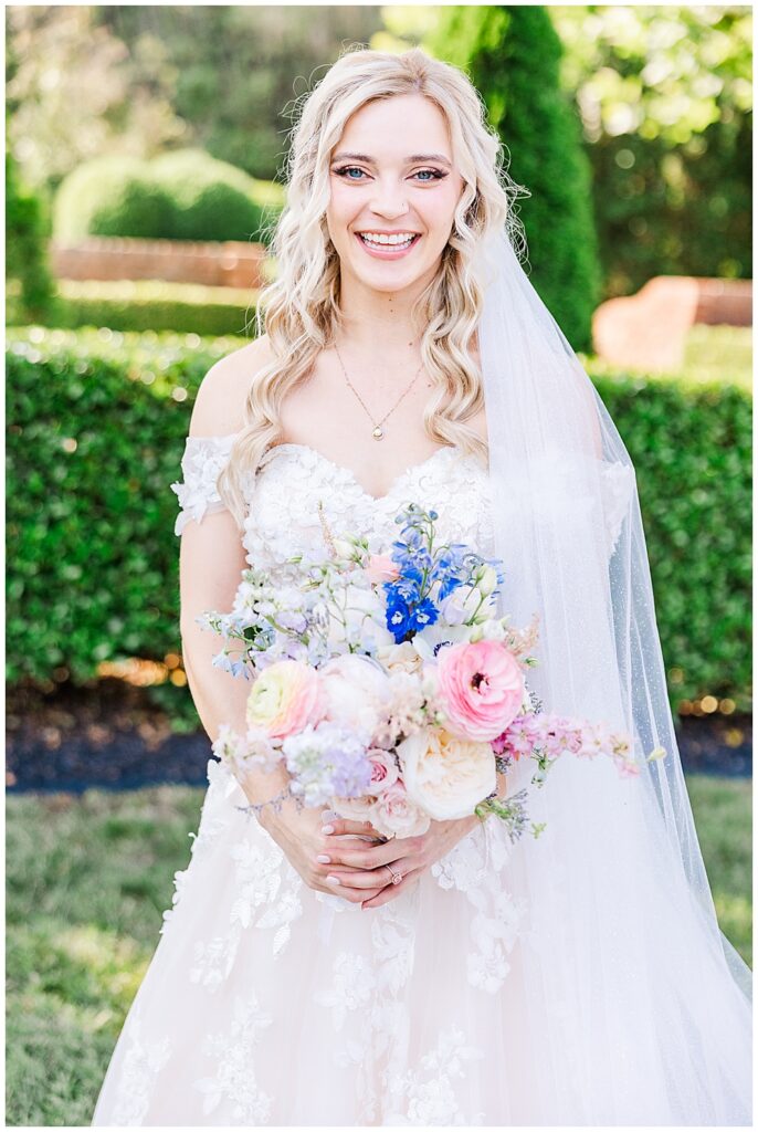 Smiling bride with blonde hair holding a bridal bouquet of assorted pastel-tone wedding flowers | Fairytale-themed Historic Mankin Mansion wedding in June | Richmond wedding photographer