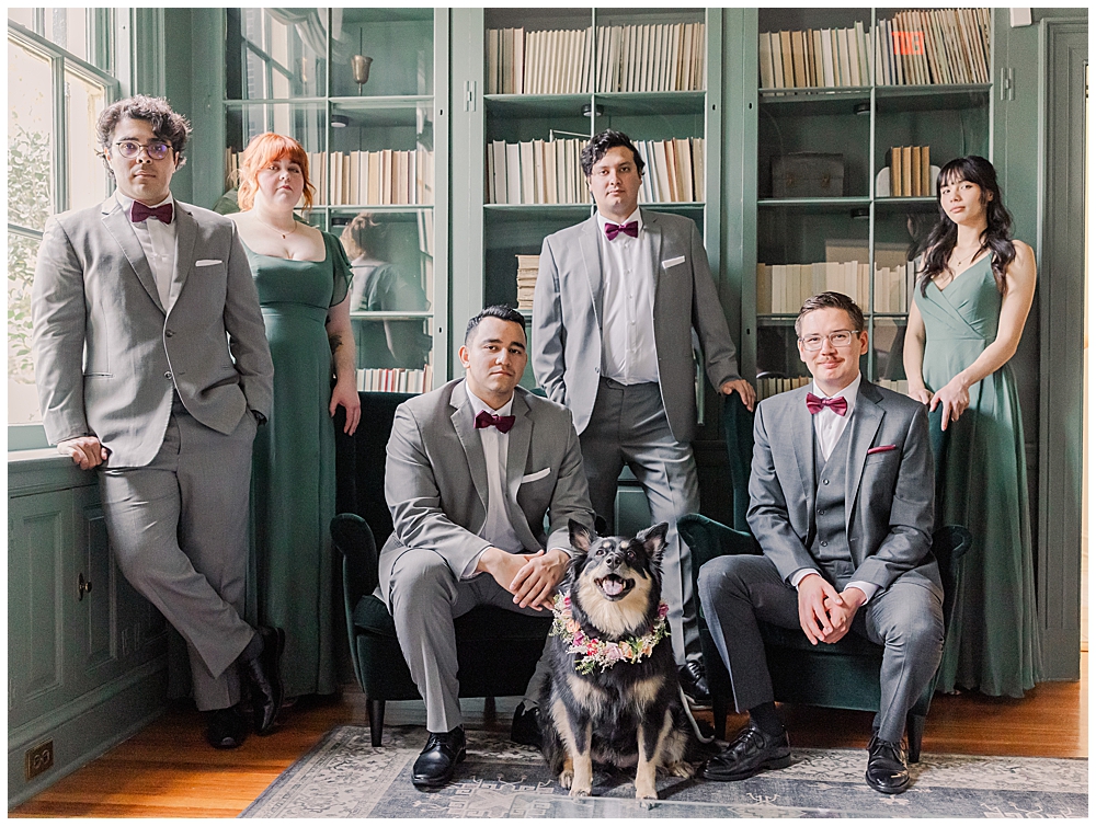 A portrait of a groom and his groomsmen & groom's friends. All are seated in a green library at Rust Manor. Four of the men are wearing grey suits and burgundy bowties and the two women are in sage green, floor length bridesmaid dresses.

Rust Manor House Wedding | Leesburg Wedding Photography | VA Wedding Venues