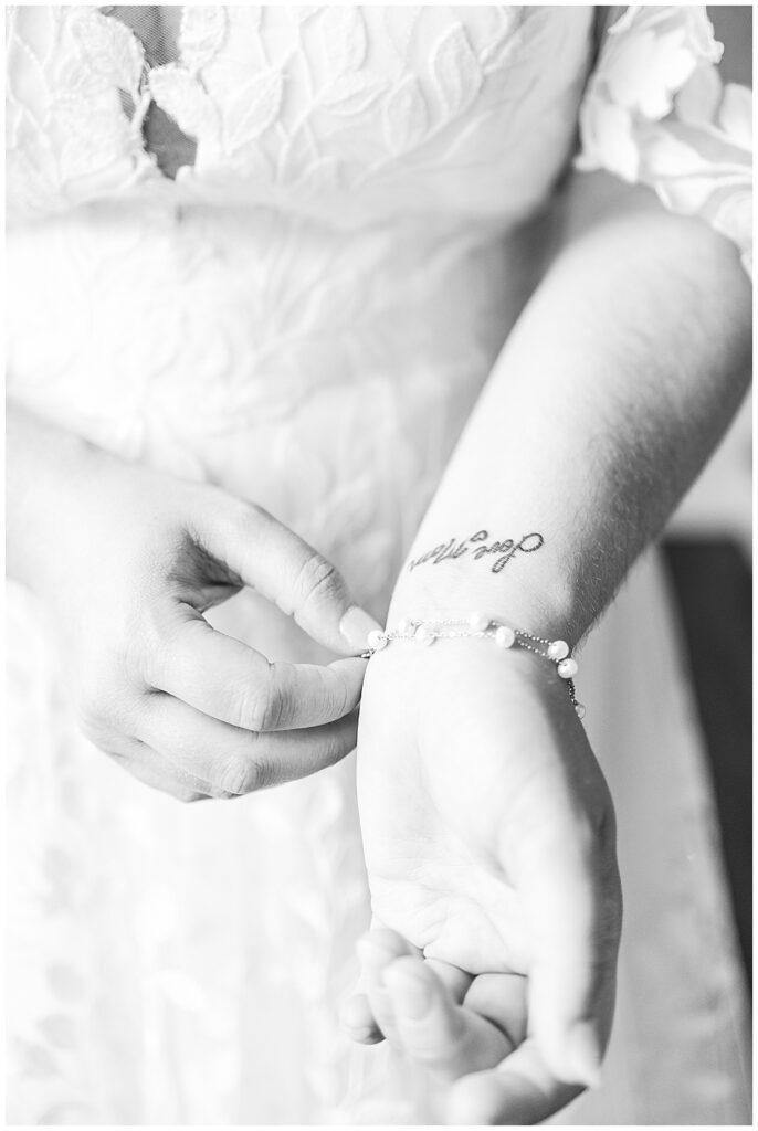 A black and whtie close-up shot of a bride putting on her pearl and silver chain bracelet. On her wrist is a tattoo honoring her late mother that says "Love, Mom" in cursive letters.

Rust Manor House Wedding | Leesburg Wedding Photography | VA Wedding Venues