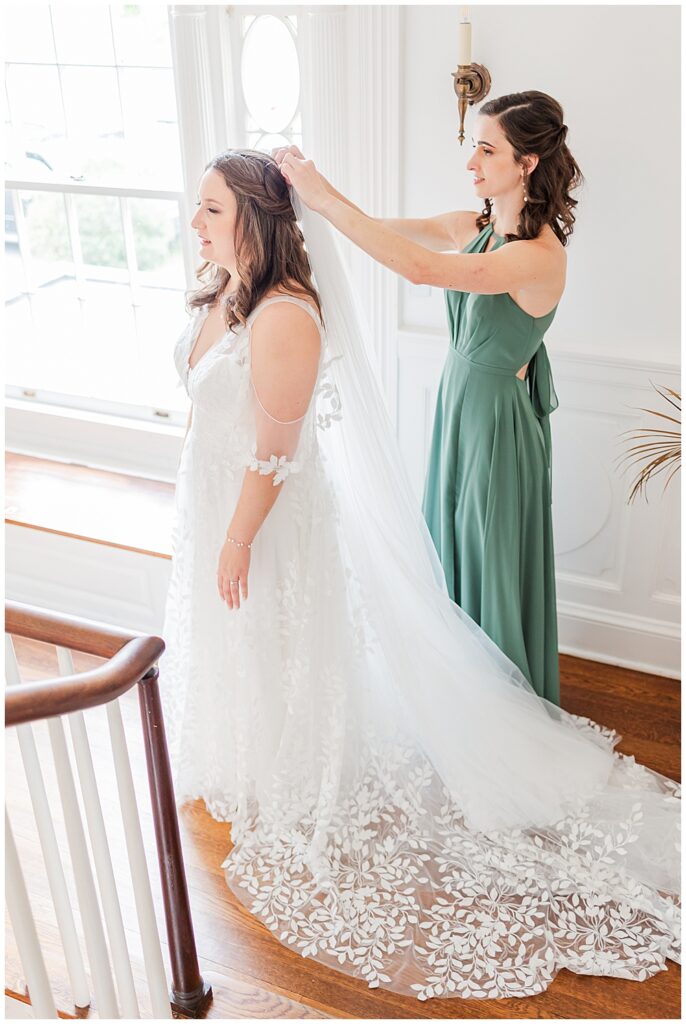 A maid of honor dressed in a sage green bridesmaid dress helps the bride put on her full-length tulle veil.

Rust Manor House Wedding | Leesburg Wedding Photography | VA Wedding Venues
