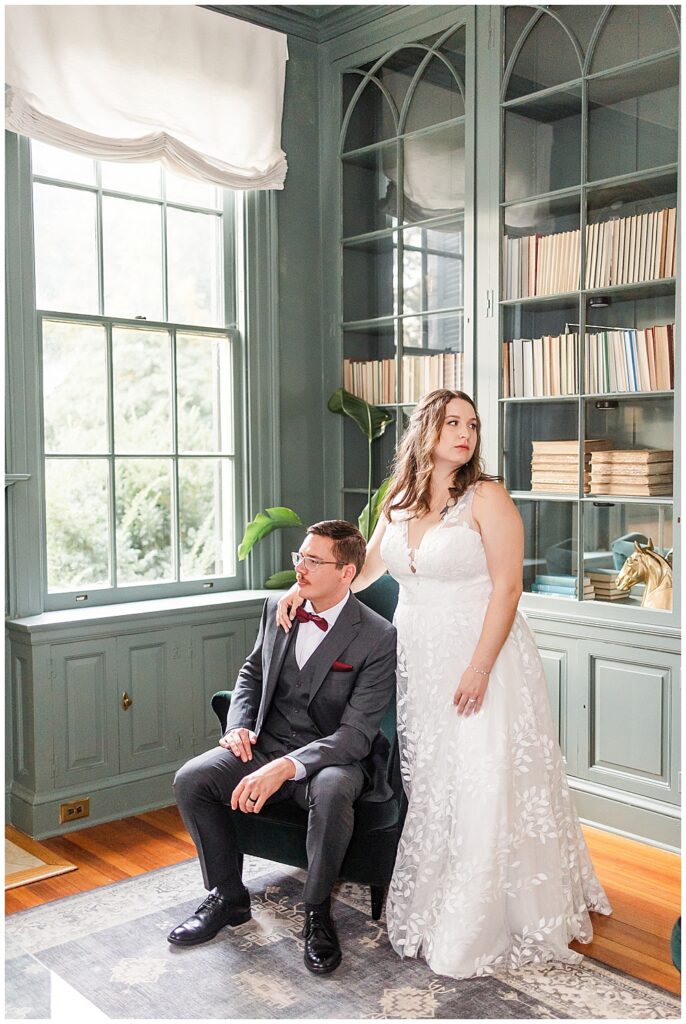 A fashion portrait of a bride and groom looking in opposite directions, the groom is seated in a velvet green chair and the bride is standing beside him. 

Rust Manor House Wedding | Leesburg Wedding Photography | VA Wedding Venues